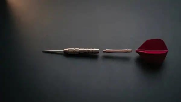 Disassembled dart showing point, barrel, shaft, and flight on dark charcoal surface