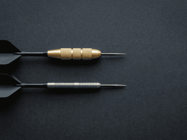 Tungsten vs brass darts barrel width comparison — thick brass barrel next to slim tungsten barrel on dark surface