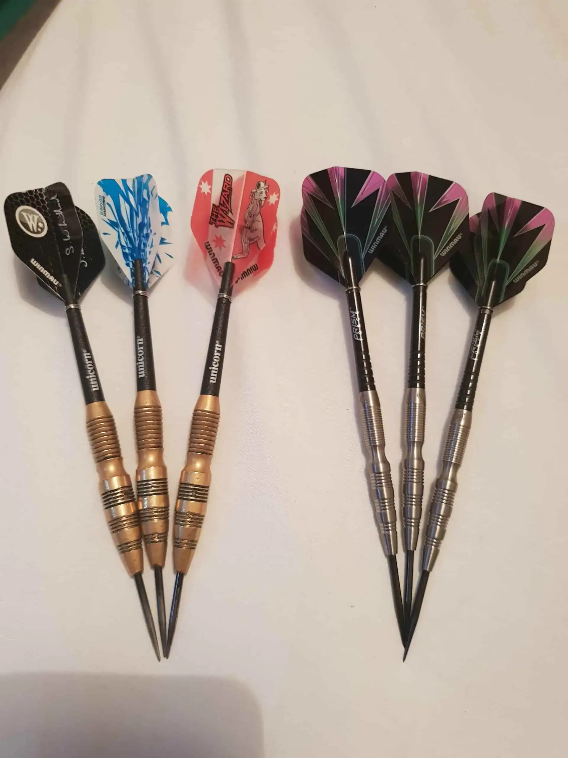 Tungsten vs brass darts barrel width comparison  -  thick brass barrel next to slim tungsten barrel on dark surface