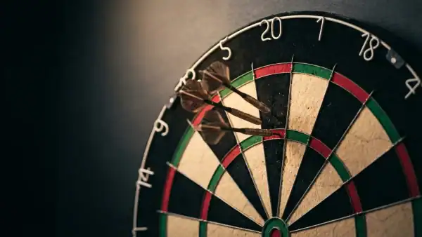 Three steel-tip darts embedded in a sisal bristle dartboard showing a checkout route, photographed from above on a dark background