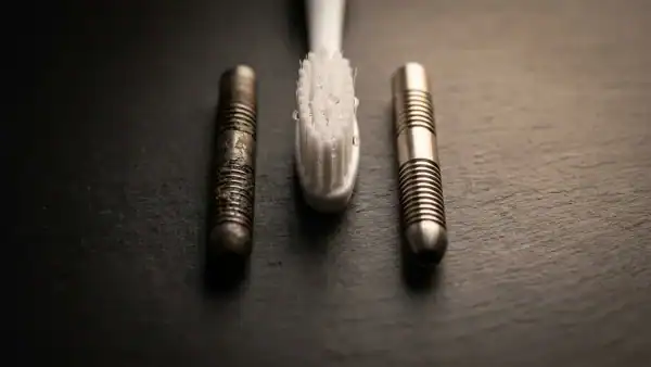 Dirty tungsten dart barrel next to a freshly cleaned barrel with a toothbrush between them