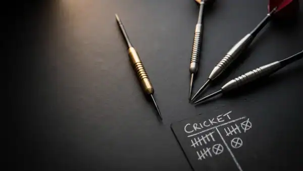 Multiple tungsten darts and a cricket scoresheet on a dark charcoal surface