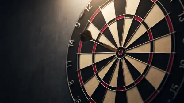 Bristle dartboard on dark wall with spotlight and embedded dart