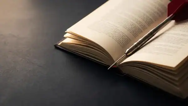 Open reference book with a steel-tip dart resting across the pages on a dark charcoal surface