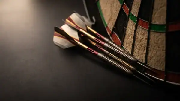 Three darts tightly grouped in a dartboard treble bed with dramatic side lighting