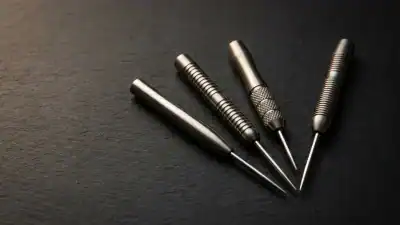Four tungsten dart barrels with steel tips in fan arrangement on charcoal surface showing different grip textures