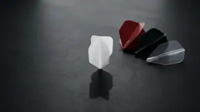 Four dart flights in different shapes and colours on a dark charcoal surface