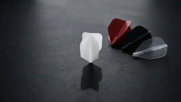 Four dart flights in different shapes and colours on a dark charcoal surface