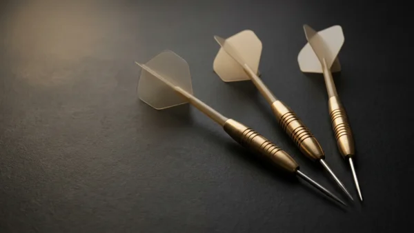 Three complete brass darts with flights stems and steel tips laid in fan arrangement on charcoal surface
