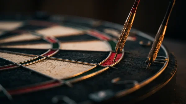 Two darts at the edge of a dartboard under a warm spotlight, one in the double bed and one just outside the wire